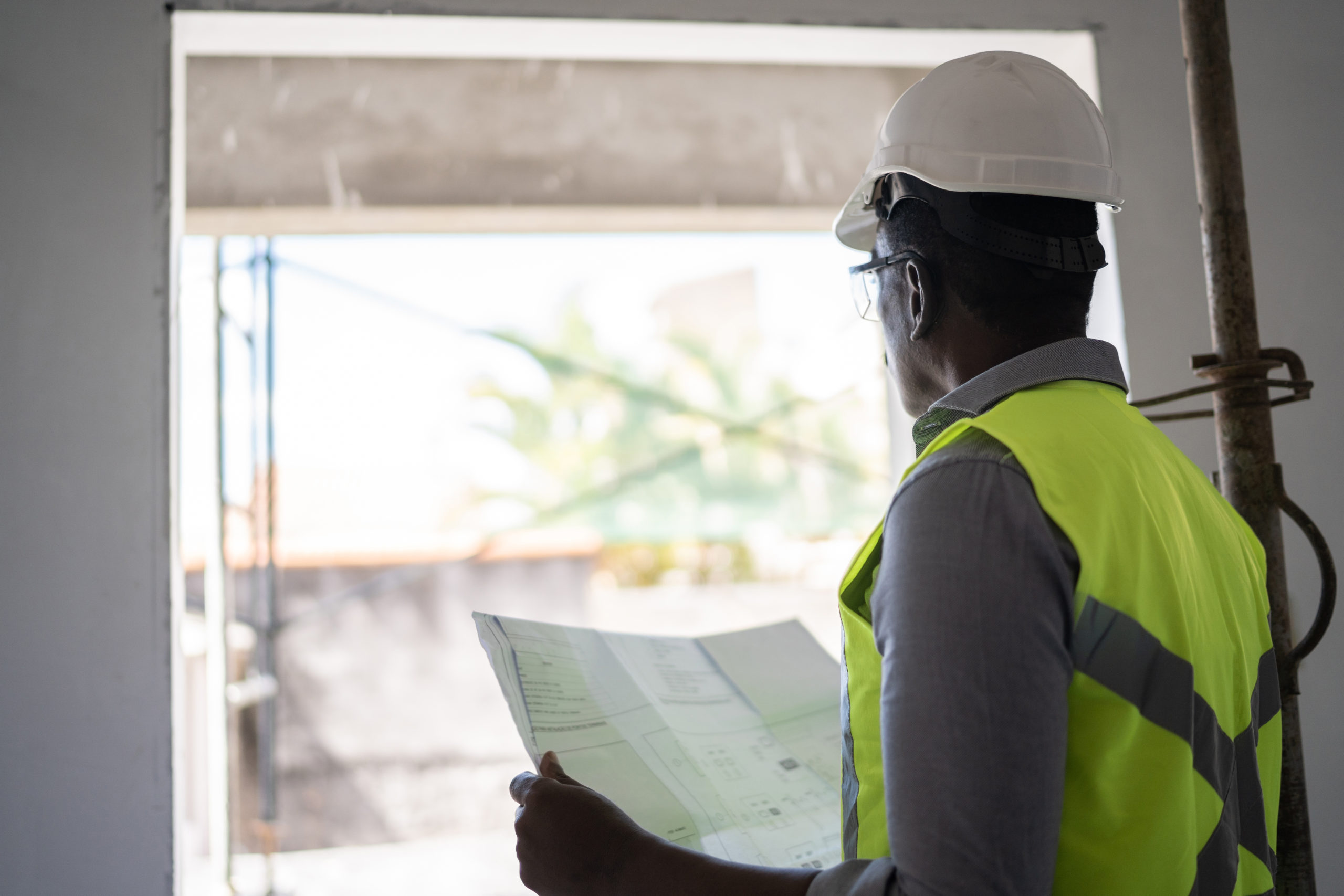 A senior construction worker is holding a blueprint and contemplating it at a construction site.